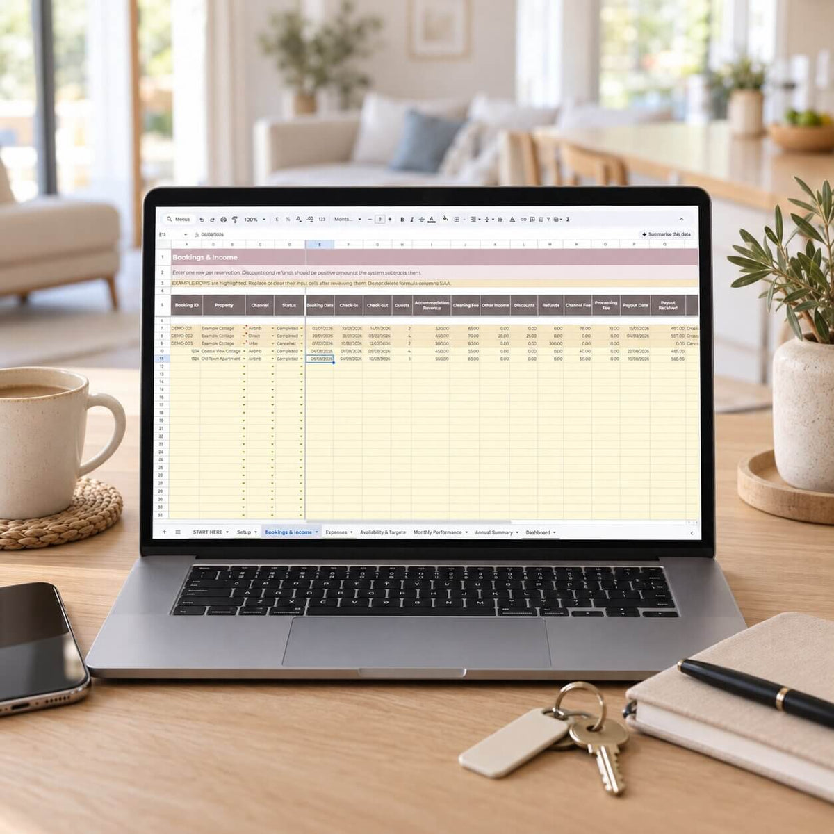 A laptop on a wooden desk displaying a spreadsheet template, surrounded by a coffee mug, smartphone, keys, notebook, and pen in a bright, modern living room setting.