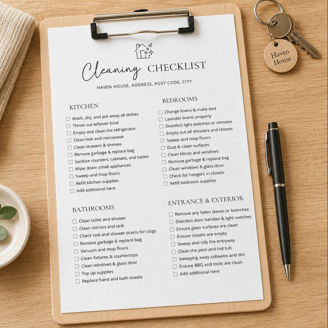 A printed cleaning checklist sheet clipped to a clipboard with a pen nearby, photographed on a wooden surface with a small plant and a key tag visible. The sheet includes sections for kitchen, bedrooms, bathrooms, and entrance/exterior with checkbox items and a small house icon at the top.