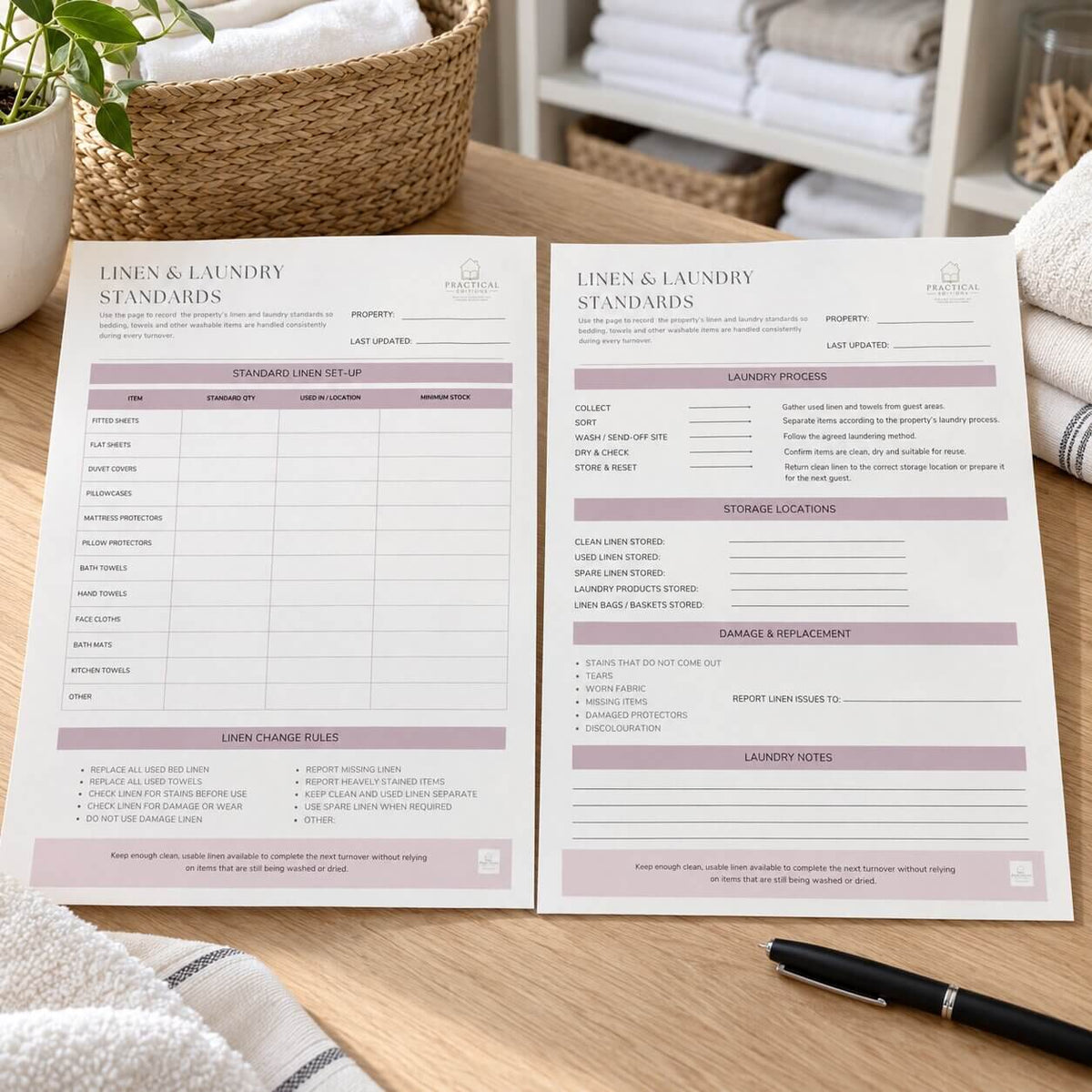 Two printed linen and laundry standards forms laid on a wooden table, with a basket, plant, folded towels, and a pen nearby. The forms are white with blush pink headings and black text.